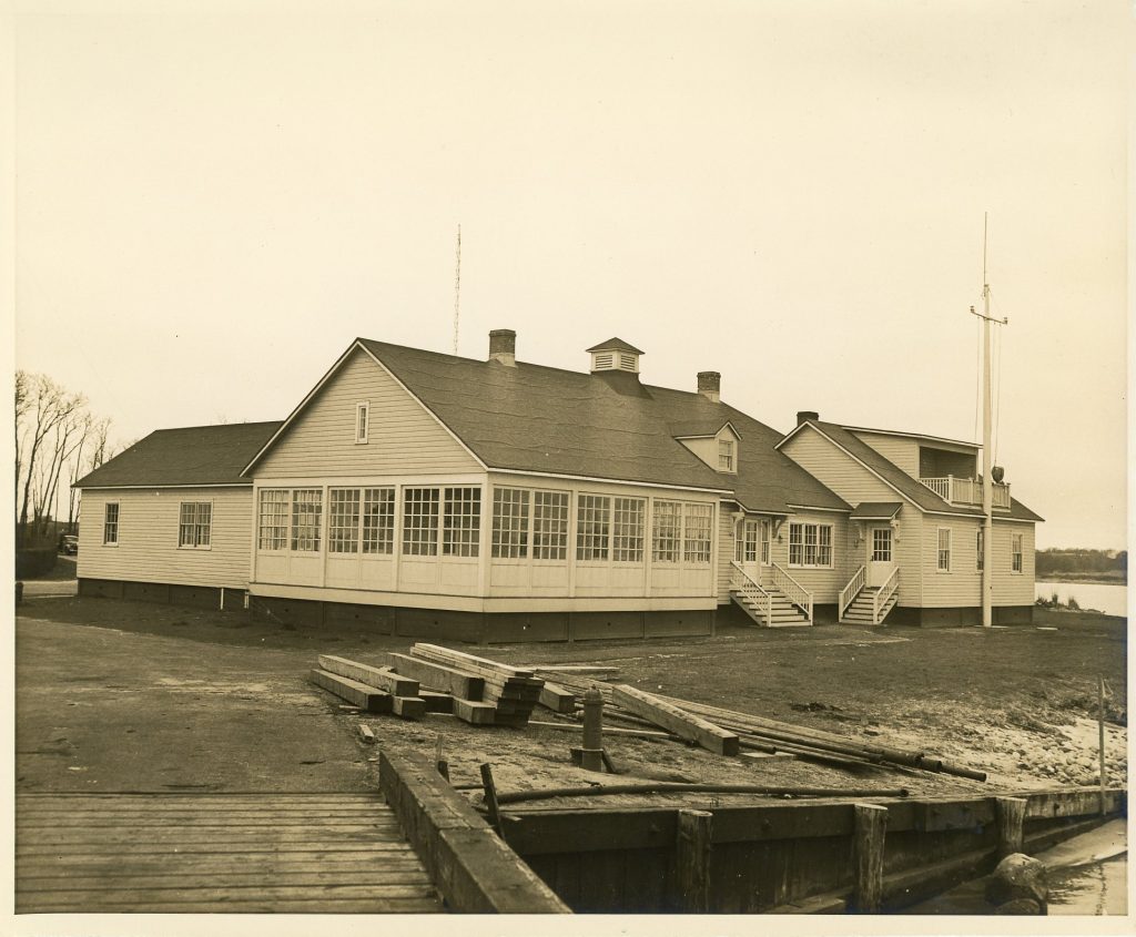 Exterior view of a barracks dormitory with windows, flagpole, and dock.