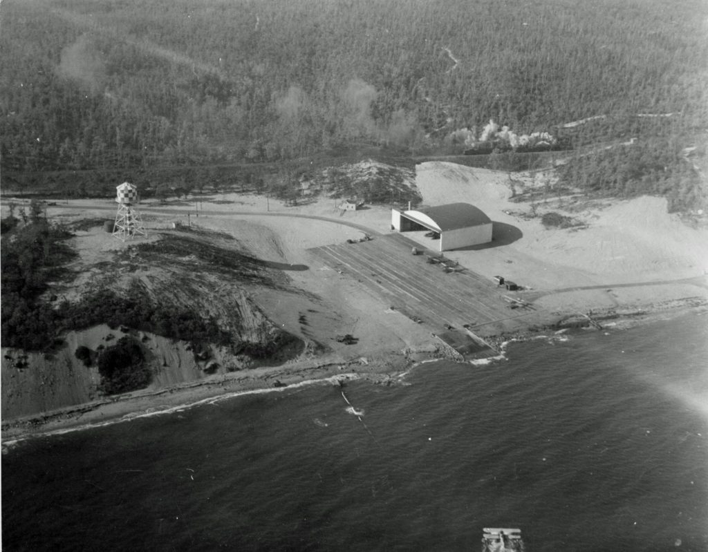 Aerial view of large building that served as seaplane hangar with adjacent dock for planes to enter or exit water. 