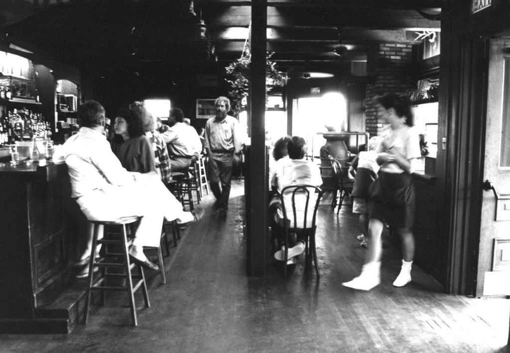A waitress and patrons at a bar and or restaurant.
